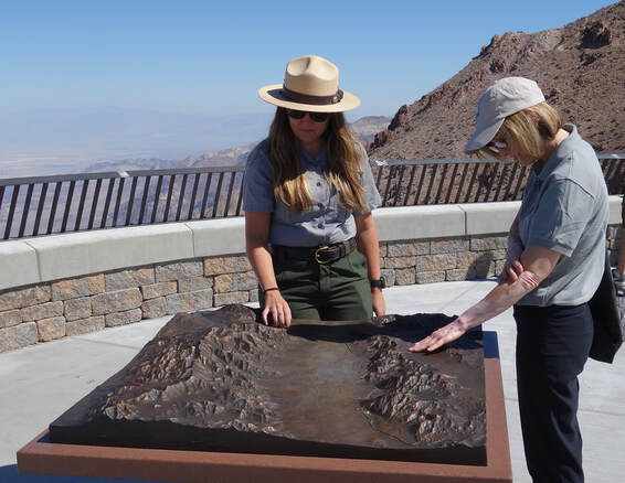 A ranger and visitor touch the bronze relief map of Badwater Basin at Dantes View